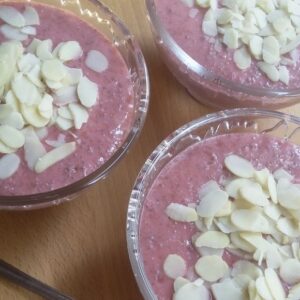 Roze chia-pudding van aardbeien in glazen kommetjes met amandelschilfers als topping.