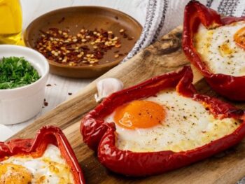 Gevulde paprika met ei - 3 halve rode paprika's met spiegelei erin - op houten plank gepresenteerd